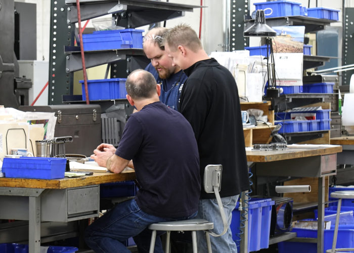 Three men working on a computer in an assembly shop.