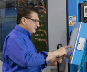 A man in blue shirt and glasses pointing to an item on display.