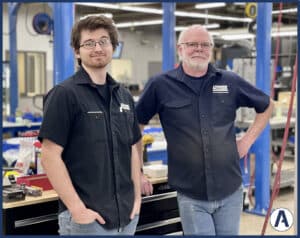 Two men standing in a garage with their hands on their hips.